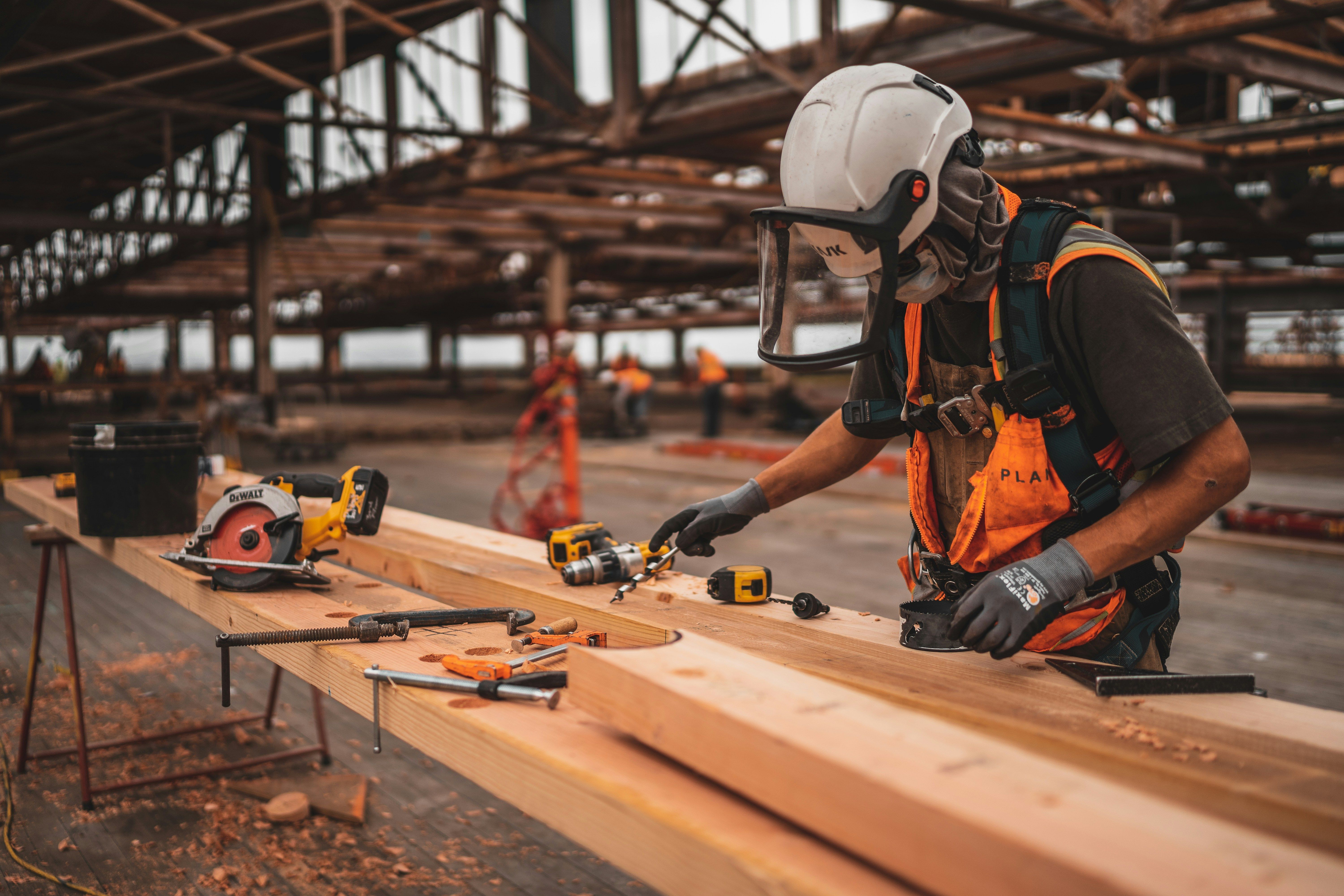 A construction worker in hi-vis and a hard hat measuring timber on a building site